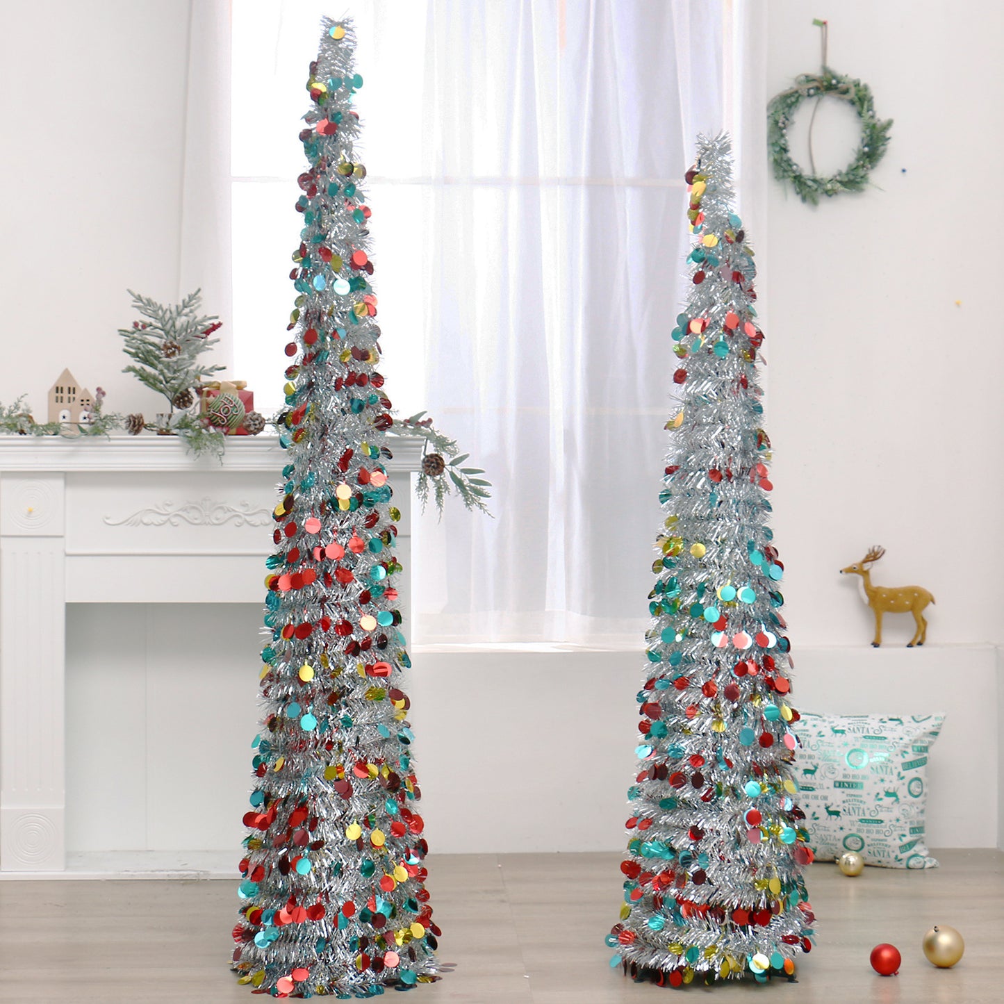 Two tall silver tinsel Christmas trees decorated with red, yellow, and blue circular ornaments in a bright room
