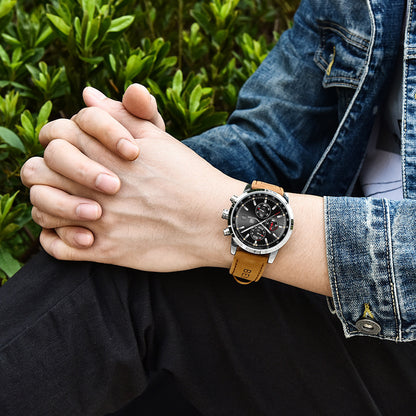 Men's quartz watch with black dial and brown leather strap worn on wrist, styled with denim jacket