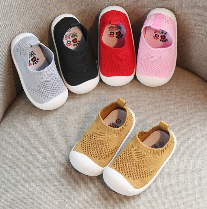 Soft sole toddler slip-on knit shoes in grey, black, red, pink, and mustard on beige fabric