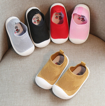 Soft sole toddler slip-on knit shoes in grey, black, red, pink, and mustard on beige fabric