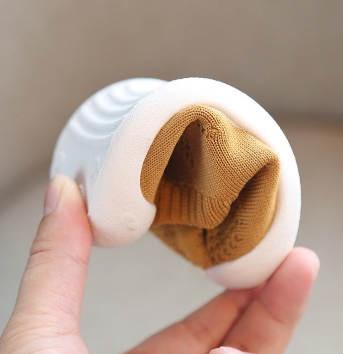 Hand holding flexible white soft sole toddler shoe with brown breathable cotton upper