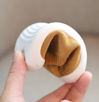 Hand holding flexible white soft sole toddler shoe with brown breathable cotton upper