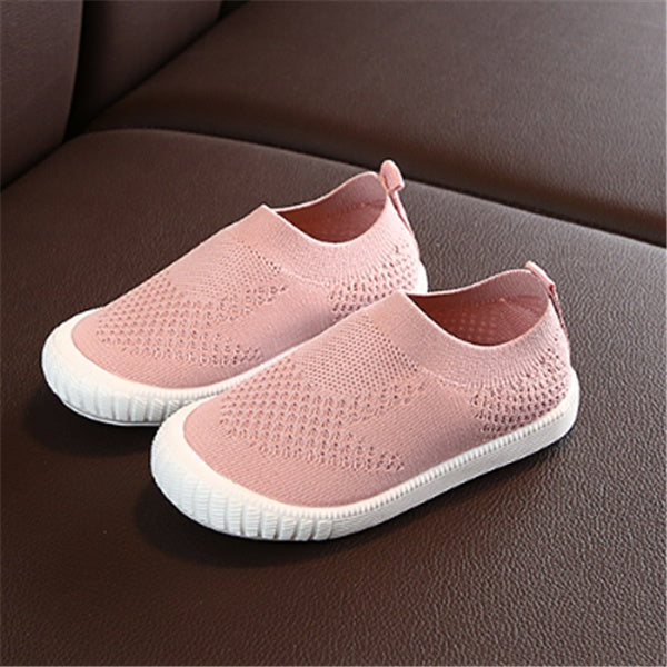 Pink toddler slip-on shoes with breathable knit fabric and white flexible soles on brown surface