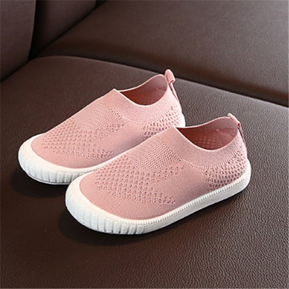 Pink toddler slip-on shoes with breathable knit fabric and white flexible soles on brown surface