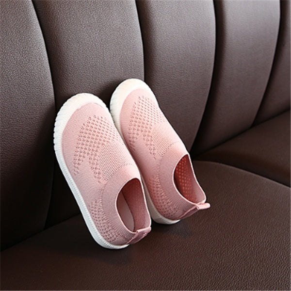 Dark pink toddler slip-on shoes with soft breathable cotton upper and flexible white soles on brown leather surface