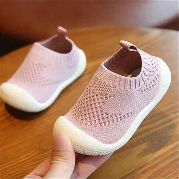 Light pink toddler slip-on shoes with breathable knit fabric and soft white soles on wooden surface