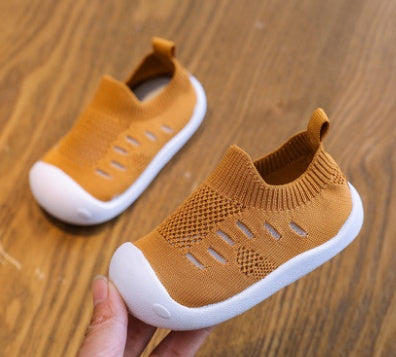 Brown toddler slip-on shoes with breathable knit fabric and flexible white soles on wooden surface