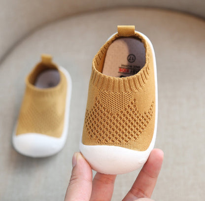 soft yellow toddler slip-on shoe with breathable knit upper and white flexible sole held in hand