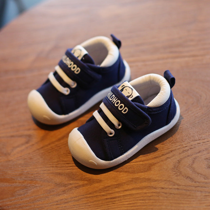 Navy blue toddler shoes with white soles and velcro straps on wooden surface, flexible baby footwear