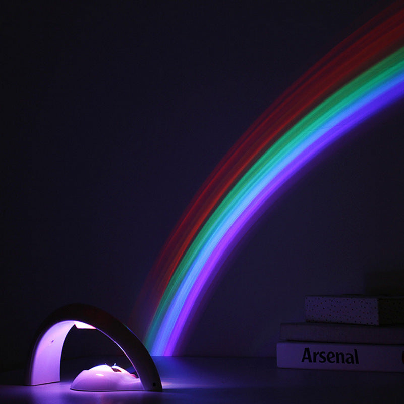 Rainbow LED night light projector casting colorful arc on dark wall with books nearby