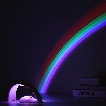 Rainbow LED night light projector casting colorful arc on dark wall with books nearby