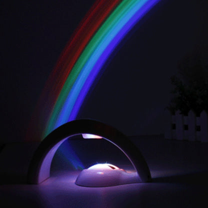 LED rainbow projector night light casting colorful arc in dark room with small white fence and plants