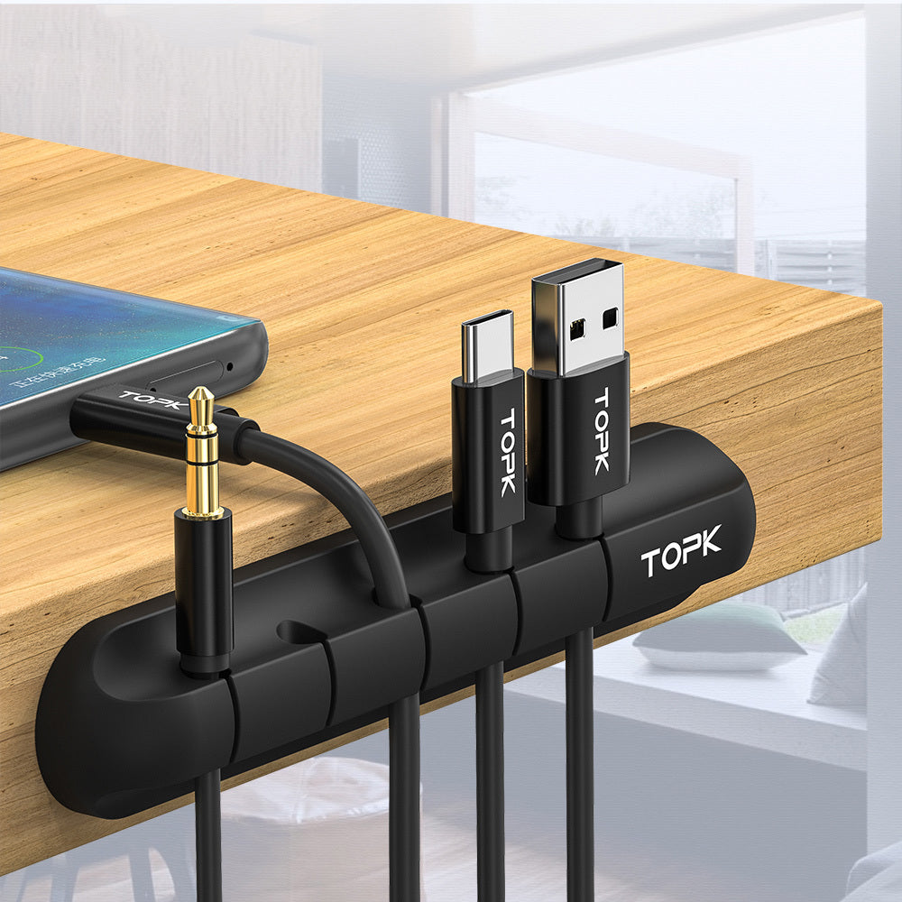 Black TOPK silicone cable organizer clipped on wooden desk holding USB, USB-C, and audio cables