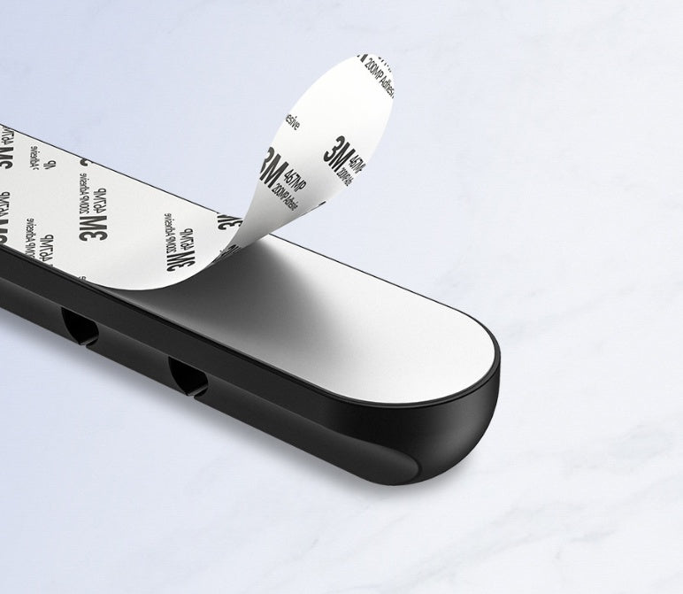 Black silicone cable organizer with 3M adhesive backing peeling off on white surface