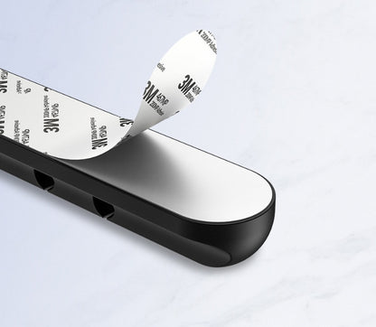 Black silicone cable organizer with 3M adhesive backing peeling off on white surface