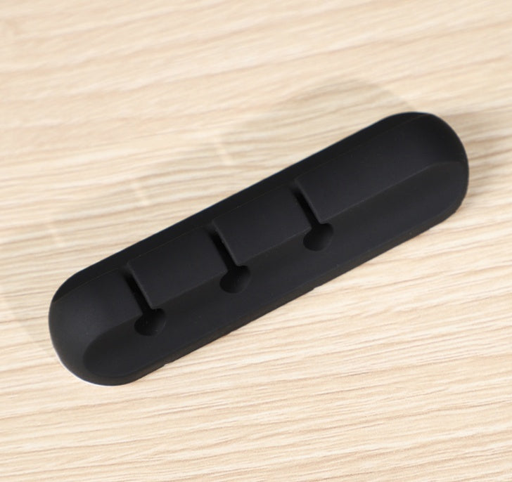 Black silicone cable organizer with three slots on light wood surface for desk wire management