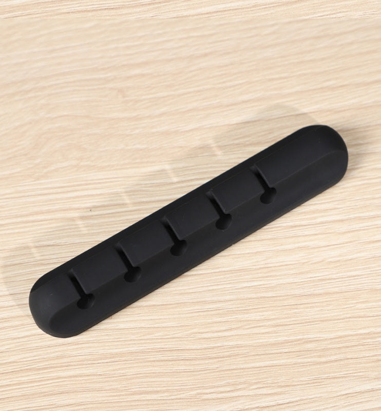 Black silicone cable organizer with five slots on light wood surface for desk wire management