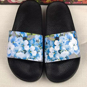 Black slide sandals with wide straps featuring blue and white floral print on textured footbed