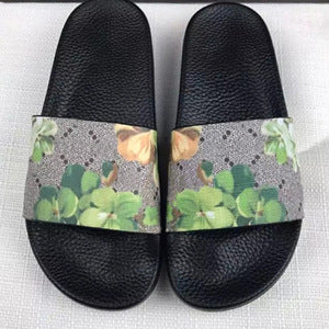 Black slide sandals with green and yellow floral patterned straps on white fabric