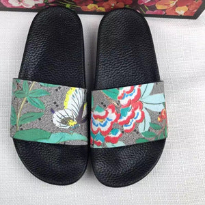 Black slide sandals with floral and butterfly printed straps on white surface