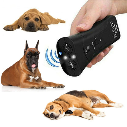 Hand holding black ultrasonic dog repeller with LED light, three dogs lying nearby