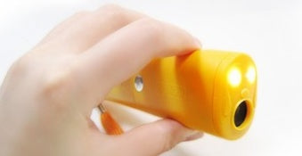 Hand holding yellow ultrasonic dog repeller with LED flashlight on white background