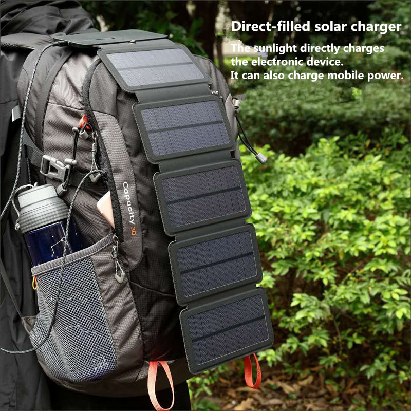 Folded portable solar charger attached to black hiking backpack outdoors with water bottle and greenery