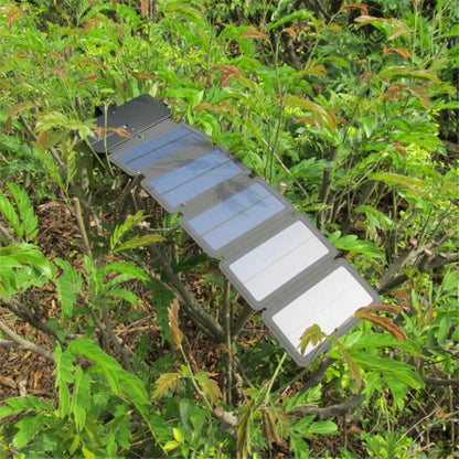 Portable foldable solar panel charger with multiple panels placed on green bush leaves outdoors