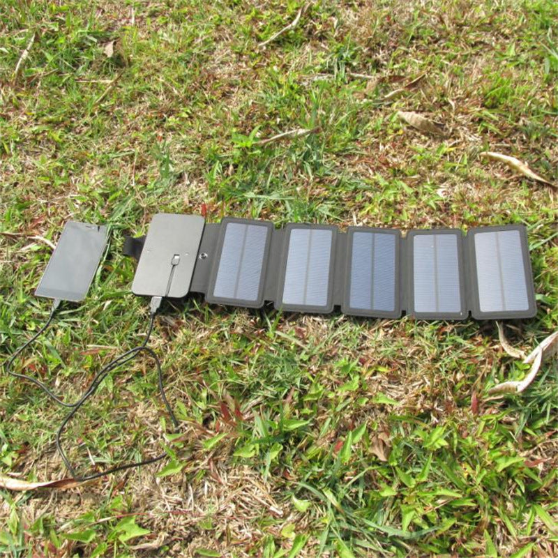 Black portable folding solar charger with five solar panels charging a device on green grass