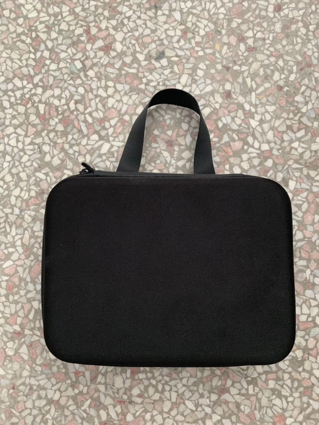 Black rectangular carrying case with handle on terrazzo floor background