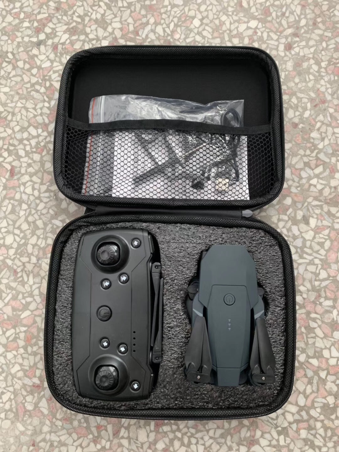 Compact black quadcopter drone and remote control stored in portable black foam case on terrazzo floor