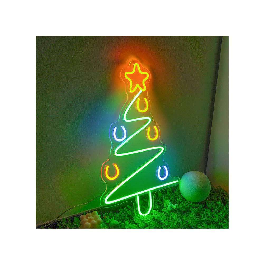 Colorful neon Christmas tree sign with star topper, horseshoe decorations, glowing indoors on green background