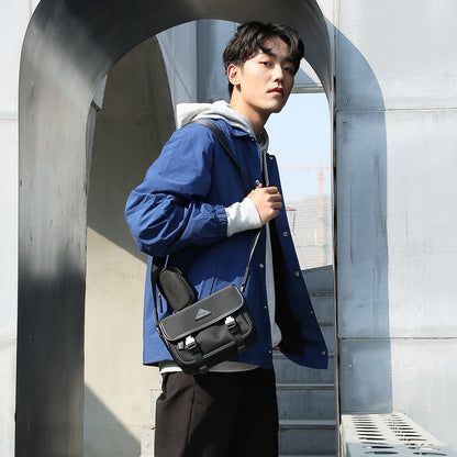 Man wearing blue jacket and gray hoodie carrying black nylon messenger bag with zipper outdoors