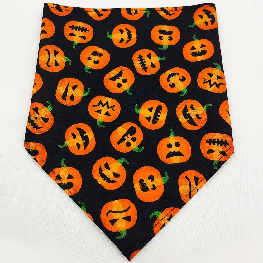 Black pet bandana with orange Halloween pumpkin faces pattern on white background