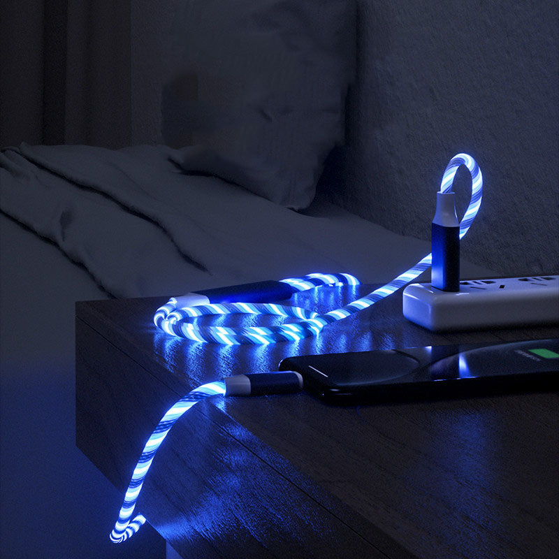 3-in-1 LED glowing charging cable connected to a smartphone on a wooden bedside table in a dark room