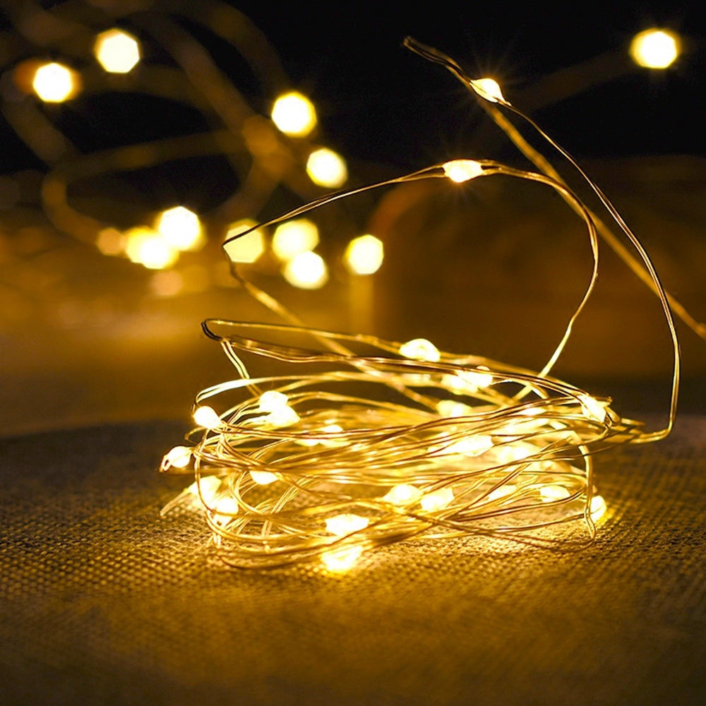 Coiled warm white copper wire LED fairy string lights glowing on textured surface in dark setting