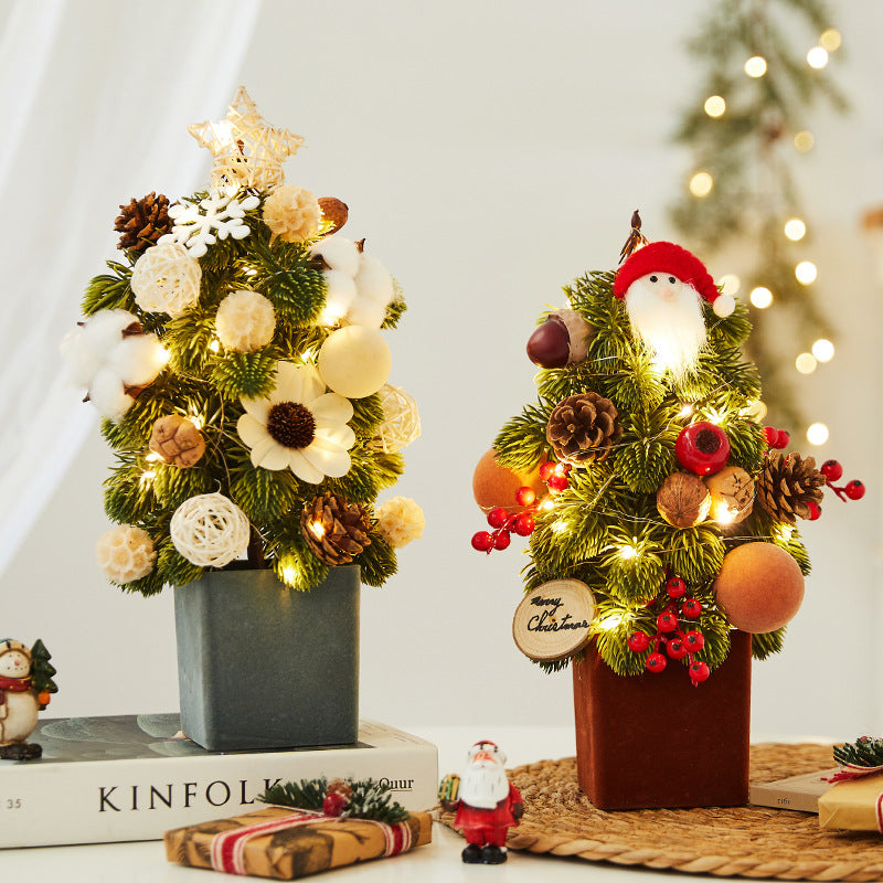 Two small festive Christmas tree decorations with pine cones, berries, cotton, and star lights on a table