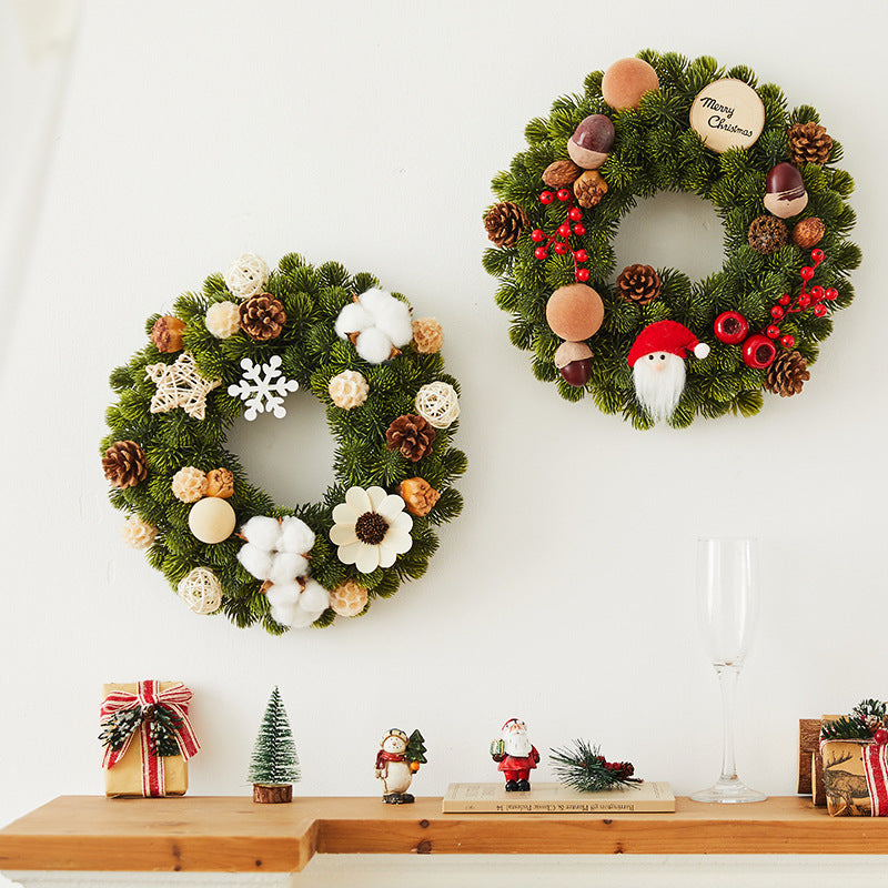 Two festive Christmas wreaths with pine cones, berries, cotton, and holiday decor on white wall above wooden shelf