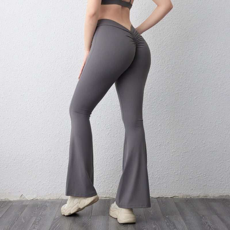 Woman wearing gray high-waist bootcut fitness pants with ruching detail, standing against white wall