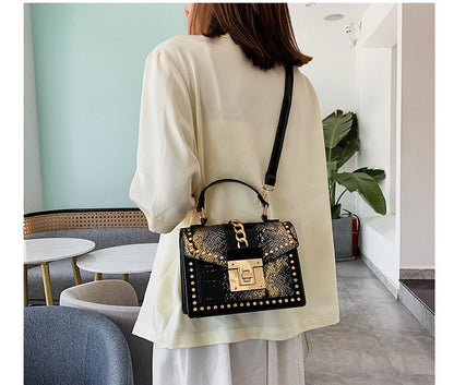 Woman wearing beige top carrying black and gold alligator-print shoulder bag with gold lock in modern cafe
