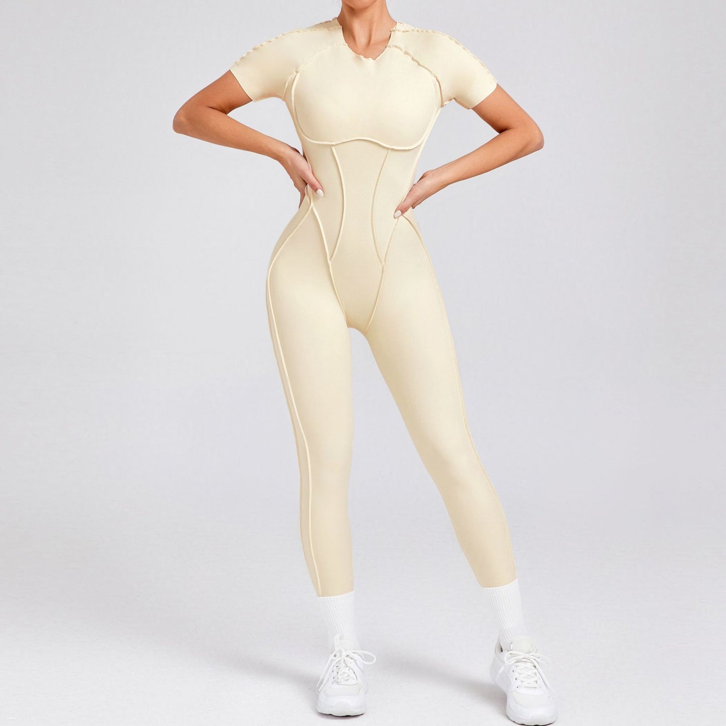 Woman wearing beige short-sleeve yoga jumpsuit with white sneakers and socks on gray background