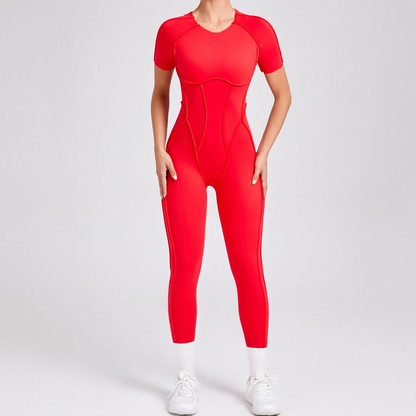 Woman wearing bright red fitted short-sleeve athletic jumpsuit with white sneakers on plain background