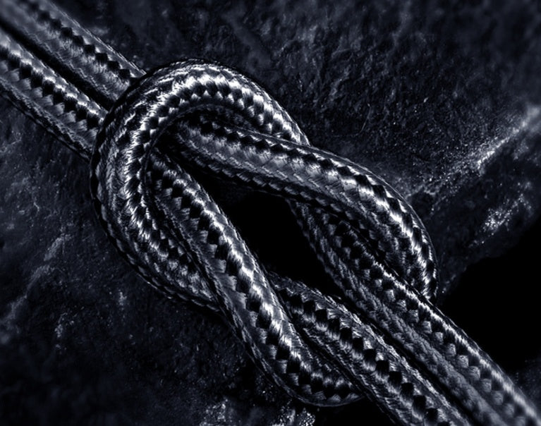 Close-up of black braided USB-C charging cable tied in a knot on dark textured surface