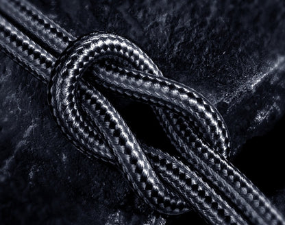 Close-up of black braided USB-C charging cable tied in a knot on dark textured surface