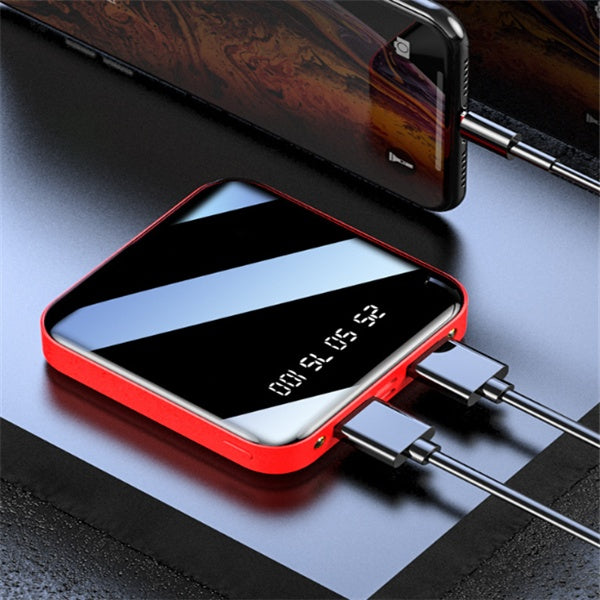 Red and black portable power bank with digital battery display charging two devices on black surface