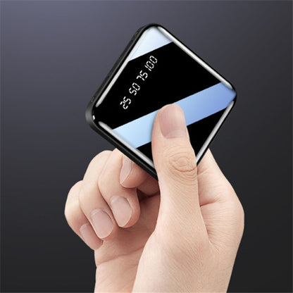 Hand holding a compact black portable power bank with digital battery display on a dark background