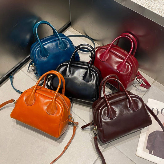 Five small leather bowling bags in orange, blue, black, red, and brown on tile floor with strap and magazine