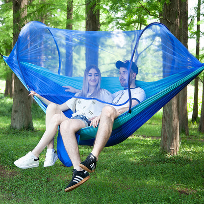 Couple sitting in blue pop-up camping hammock with mosquito net in forest setting