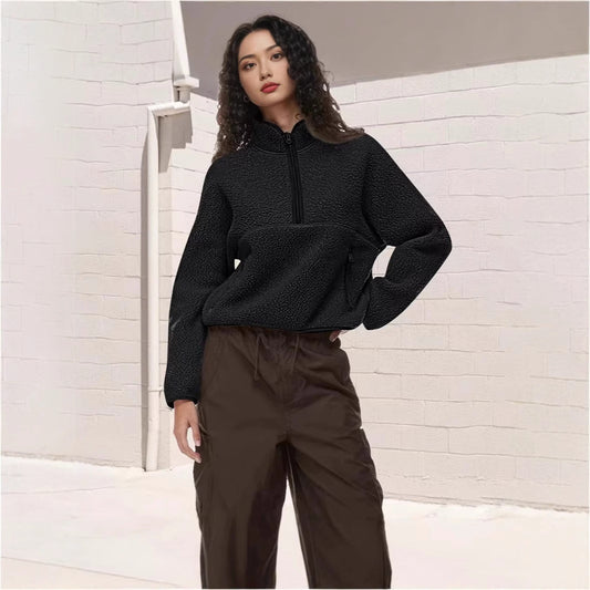 Woman wearing black half-zip lamb wool sweatshirt and brown loose pants against white brick wall