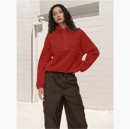 Woman wearing red fleece half-zip sweatshirt and black loose pants against white brick wall